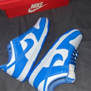 Nike Dunk i blått och vitt - Säljer ett par snygga Nike Dunk sneakers i blått och vitt. Skorna har en klassisk design med snörning och en bekväm passform. Perfekta för både vardag och träning!i storleken 43 köpte den helt nya här på Plick men har inte använt för dem var stora . 
