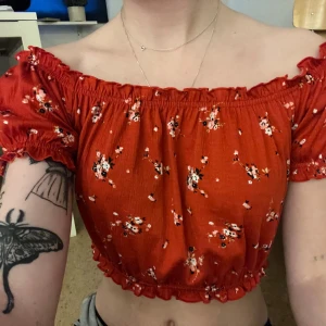 Röd blommig offshoulder topp från H&M - Säljer en superfin röd offshoulder topp från H&M med små blommor i vitt och rosa. Toppen är croppad och har korta puffärmar. Perfekt för sommaren och festliga tillfällen! 🌸