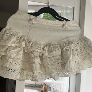 Vit kjol med volanger från River Island - Säljer en superfin vit kjol från River Island. Den har en söt volangdetalj och en dragkedja bak. Perfekt för sommaren eller en festlig dag! Kjolen är i bra skick och har en romantisk stil med broderade detaljer.