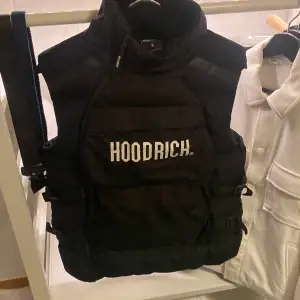 Säljer en snygg svart dunväst från Hoodrich i storlek S. Västen har en cool design med dragkedja och är perfekt för höst och vinter. Den är quiltad för extra värme och stil.