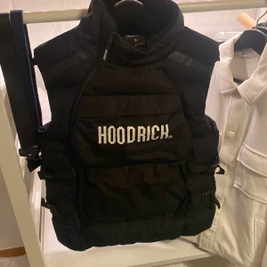 Svart dunväst från Hoodrich - Säljer en snygg svart dunväst från Hoodrich i storlek S. Västen har en cool design med dragkedja och är perfekt för höst och vinter. Den är quiltad för extra värme och stil.