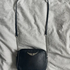 Svart axelväska från Zadig & Voltaire - Säljer en snygg svart axelväska från Zadig & Voltaire. Väskan är i skinn och har en cool silverfärgad kedja som axelrem. Knappt använd, dustbag och kvitto finns (nypris 1990kr). 