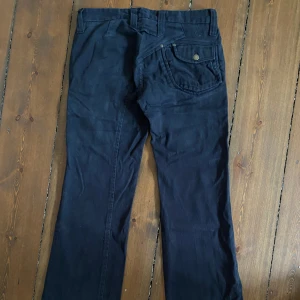 Flared svarta jeans - Vintage jeans från J Lindeberg med skön utsvängd men också lite baggy passform. De har riktigt najs design på baksidan. De är avklippta där nere