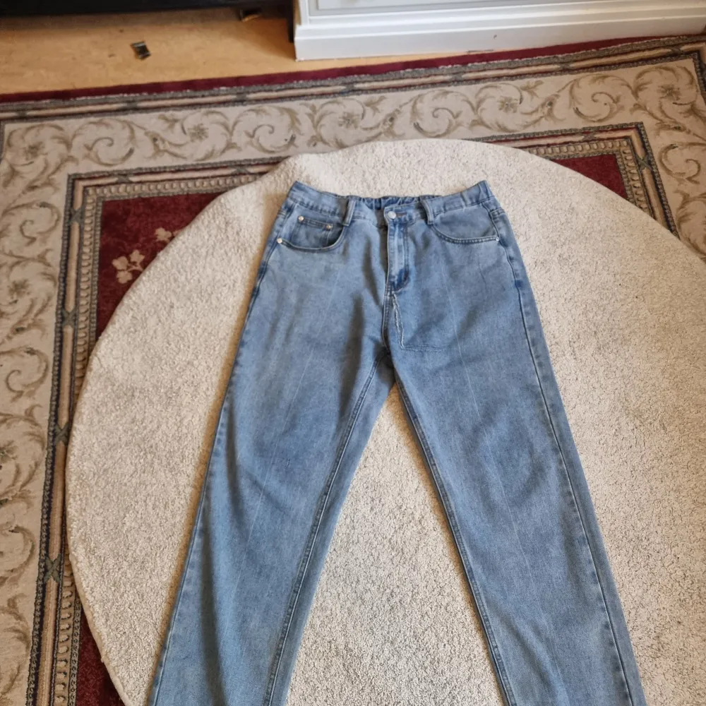 Säljer ett par klassiska blå jeans från Newtusfan i storlek 34. De har en straight passform och är tillverkade i bomull och polyester. Perfekta för vardagsbruk med en bekväm midja och traditionella fem fickor. Den är lite baggy. Jeans & Byxor.