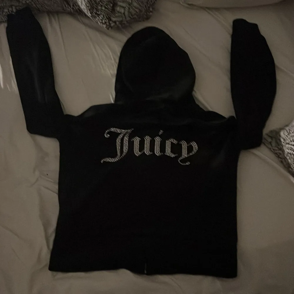 Säljer en svart hoodie från Juicy Couture med dragkedja och huva. Den har långa ärmar och texten 'Juicy' i glittriga bokstäver på ryggen. Perfekt för en avslappnad och stilren look!. Hoodies.