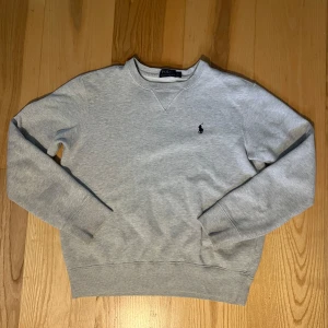 Ralph lauren sweatshirt  - Jättefin ralph tröja i grått. Den är i väldigt fint material och är perfekt nu till hösten. Den säljs då den inte har använts på något år då den varit för liten. Det finns en defekt (se bild 4/5) därav det billiga priset..