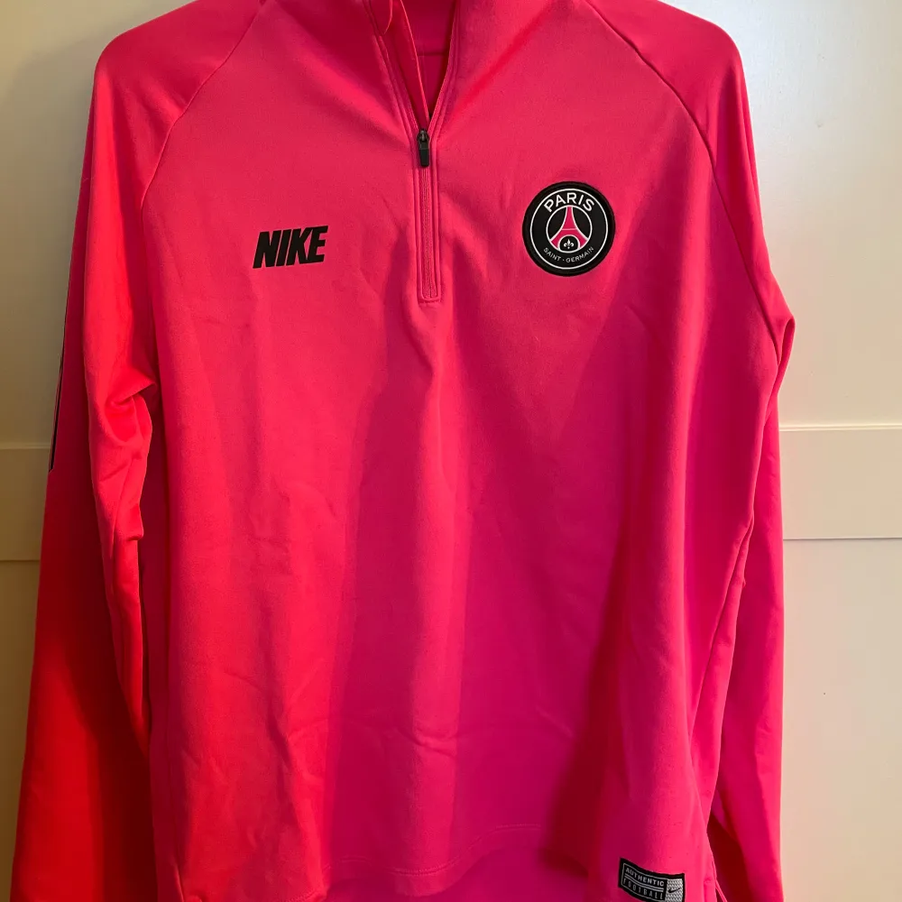 Säljer en snygg rosa långärmad tröja från Nike med PSG-logga på bröstet. Tröjan har en halv dragkedja framtill och är perfekt för träning eller vardagsbruk. Materialet känns mjukt och bekvämt.. Tröjor & Koftor.