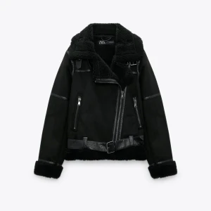 Svart jacka med fuskpäls från Zara - Säljer en supercool svart jacka från Zara med fuskpälsdetaljer. Den har en asymmetrisk dragkedja och ett bälte i midjan för extra stilpoäng. Jackan är perfekt för höst och vinter, och den har långa ärmar med päls vid ärmsluten. Den är både snygg och varm, perfekt för att hålla stilen i kylan!