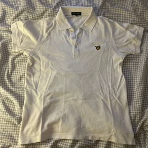 Vit pikétröja från Lyle & Scott - Säljer en klassisk vit pikétröja från Lyle & Scott. Den har korta ärmar och en liten broderad logga på bröstet. Perfekt för en stilren och avslappnad look!