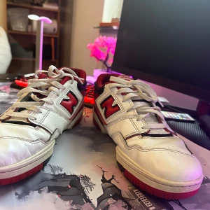 New Balance 550 sneakers i vitt och rött - Säljer ett par New Balance 550 sneakers i vitt och rött. Skorna har en klassisk design med snörning och en bekväm passform. De är i välanvänt skick men fortfarande snygga och funktionella. Perfekta för vardagsbruk eller träning.