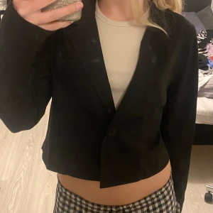 Croppad kavaj - Av kroppad svart kavaj med 1 knapp Välanvänd  Finns en extra knapp om den gamla skulle släppa 65% polyester  35% viskos