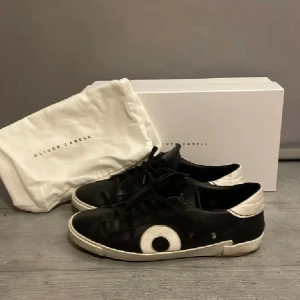 Svarta och vita sneakers från Oliver Cabell - Snygga svarta sneakers med vita detaljer från Oliver Cabell. Det är bra skick ( 8/10 ) och defekterna på skon är att en liten bit av undersidan av hälen har gått av fast har fixat den hos en skomakare. Tar gärna emot byten också!