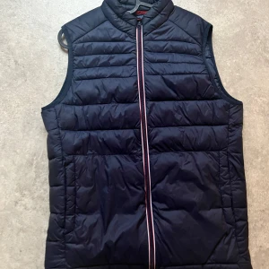 Svart quiltad dunväst - Snygg svart quiltad dunväst med dragkedja framtill. Perfekt för lager-på-lager under kyliga dagar. Västen har en stilren design med horisontella sömmar och hög krage.