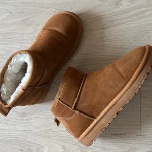 Bruna boots med foder  - Säljer ett par mysiga bruna boots med fluffigt vitt foder. En enkel design och lätta att ta på. Uggsliknande men från märket fashion. Säljer då de tyvärr är små i storleken, de är i storlek 40 men passar mer 39 eller 38. Väldigt sköna men tyvärr lite för små för mig, därav endast använda ett fåtal gånger.