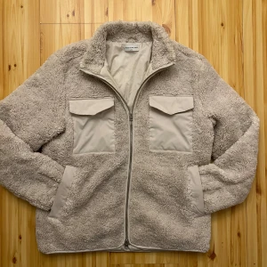 Beige teddyjacka från These Glory Days - Mysig beige teddyjacka från These Glory Days med dragkedja och två bröstfickor med lock. Jackan har en mjuk och fluffig yta, perfekt för kyliga dagar. Insidan är fodrad med Thermore för extra värme. En stilren och bekväm jacka för alla tillfällen. Nypris ca 2000kr. Den har använts sparsamt och är i nyskick! Hör av dig vid funderingar/diskutera om priset😄