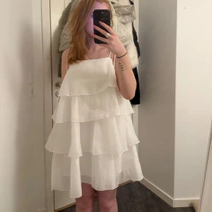 Vit klänning med volanger från ginatricot - Säljer en söt vit klänning från ginatricot med flera lager av volanger. Jättefin till student osv lappar är kvar. 