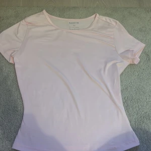 Ljusrosa t-shirt från SHEIN - Säljer en ljusrosa t-shirt från SHEIN i storlek XS. T-shirten är kortärmad och tillverkad i ett mjukt syntetmaterial. Perfekt för en avslappnad stil.