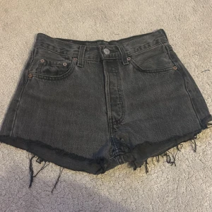Svarta jeansshorts från Levi's - Snygga svarta jeansshorts från Levi's med fransiga kanter och klassisk femficksdesign. Perfekta för en avslappnad stil. De har en knapp och dragkedja framtill.