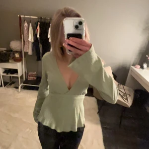 Grön topp med knytband - Snygg grön topp med långa ärmar och knytband i midjan. Perfekt för en stilren look. Toppen har en v-ringad design som ger en elegant touch.