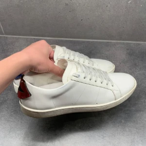 Saint Laurent, läppar - Snygga vita sneakers från Saint Laurent med unika detaljer i form av röda och blå läppar på hälen. Knappt använda. Nypris 5750kr mitt pris 2100kr