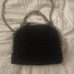 svart virkad väska med kedja  - Snygg svart stickad axelväska med en cool kedja. Perfekt för att ge din outfit en edgy touch. Väskan har en unik stickad design som liknar stella väskan