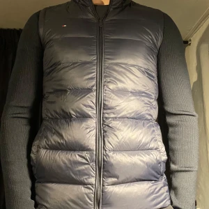 Mörkblå pufferjacka från Tommy Hilfiger - Säljer en snygg mörkblå pufferjacka från Tommy Hilfiger. Jackan har långa ärmar och en dragkedja framtill. Perfekt för kyligare dagar med sin quiltade design som håller värmen. Litet håll på framsidan märks inte när man har på sig den. 
