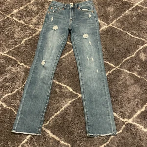 Blå jeans från Levi's - Snygga blå Levi's jeans med hög midja och rak passform. De har slitna detaljer för en trendig look och är perfekta för en avslappnad stil. Klassisk femficksdesign och knappgylf.