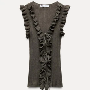 Populär grön volangtopp från Zara - Säljer en brun ribbad topp från Zara med volangdetaljer längs ärmarna och framtill. Toppen har en v-ringning och knytband framtill. Perfekt för en stilren look!