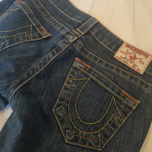 True religion blåa jeans w24  - Snygga blå jeans från True Religion med ikonisk bakficka och orangea sömmar. Tillverkade i USA, dessa jeans har en klassisk design med knapp och dragkedja framtill. Skriv för fler bilder eller frågor. 💓 Innerbenslängd: ca 75-77 cm 