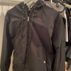 Svart vindjacka från Moncler - Säljer en stilren svart vindjacka från Moncler med dragkedja och justerbar huva. Jackan har snygga detaljer som logotyp på ärmen och moncler färgerna på luvan. Perfekt för blåsiga dagar. Priset är inte hugget i sten!!💙🤍❤️