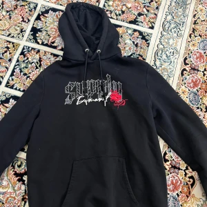 Svart hoodie från Supply & Demand - Säljer en svart hoodie från Supply & Demand med tryck på framsidan. Hoodien har en justerbar huva med dragsko och en stor ficka framtill. Perfekt för en casual look!