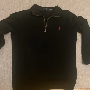 Svart tröja med dragkedja från Ralph Lauren i storlek s  - Säljer en stilren svart tröja från Ralph Lauren i storlek s med en liten röd broderad logotyp på bröstet. Tröjan har en dragkedja vid halsen och långa ärmar. 