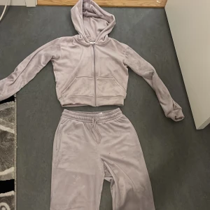 Ljus lila hoodie och byxor från H&M - Mysig ljus lila hoodie och matchande byxor från H&M. Hoodien har dragkedja och en bekväm passform med långa ärmar. Byxorna har resår i midjan för extra komfort. Perfekt för en avslappnad dag hemma eller ute.