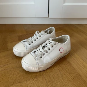 Vita sneakers från Sandro - Snygga vita sneakers från Sandro med snörning och en unik design på sulan. Skorna har en rund tå och är tillverkade i skinn med en röd logotyp på sidan. Mycket bra skick med få skrapor på framsidan. Köpta för 116euro (ca1350kr)