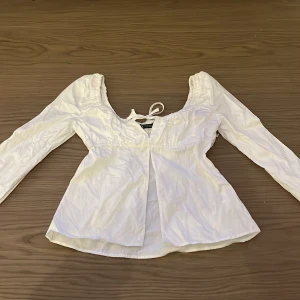 Vit blus från Zara - Säljer en söt vit blus från Zara med långa ärmar och en knytning framtill. Blusen har en elastisk detalj vid halsen och är perfekt för en stilren look. Passar bra till både jeans och kjol. Säljer den då den är för liten🤍