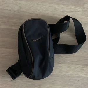 Nike crossbody väska - Liten crossbody väska från Nike, helt oanvänd. Svart med små bruna detaljer