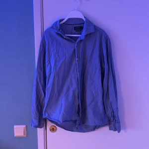 Blå skjorta från Polo Ralph Lauren - Säljer en klassisk blå skjorta från Polo Ralph Lauren. Skjortan har långa ärmar och knappar framtill. Perfekt för en stilren look.