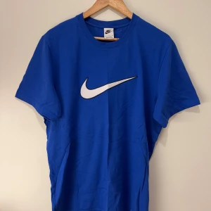 Blå t-shirt från Nike - Snygg blå t-shirt från Nike med det ikoniska swoosh-loggan i vitt på bröstet. Den har perfekt skick aldrig använt fick den som en gåva. Inget fel på den om du vill veta mer skriv i dm, säljs BILLIGT!