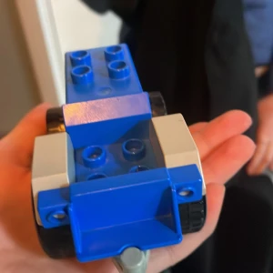 Blå och grå leksakstraktor - En söt liten leksakstraktor i blått och grått med svarta hjul. Perfekt för lekstunden och att bygga med. Traktorn har en enkel design med plats för att fästa fler byggklossar ovanpå.