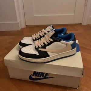 Travis Scott fragments i svart, vit och blå - Snygga Nike Air sneakers i en stilren kombination av svart, vit och blå. Skorna har klassisk snörning och en bekväm passform. Perfekta för dig som vill ha en sportig och trendig look.