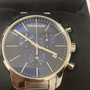 Calvin Klein herrklocka med blå urtavla - Elegant herrklocka från Calvin Klein med en stilren blå urtavla och silverfärgade detaljer. Klockan har tre subdials och en polerad metallarmband. Perfekt för den som söker en tidlös accessoar med schweizisk precision. Klockan har inget batteri men fungerar med en utan skador hämtas i kungälv det går att köpa ett nytt för 50 spänn,tar endast emot kontant