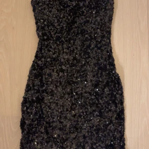 Svart paljettklänning - Snygg svart axelbandslös klänning täckt med glittriga paljetter. Perfekt för en utekväll eller fest. Från Nelly. Aldrig använd och säljer pga att den bara hänger i garderoben 🩷priset kan diskuteras