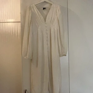 Vit långklänning med knappar - Vit midi klänning med v-ringning och långa ärmar. Klänningen har fina knappar framtill och ett diskret prickigt mönster. Perfekt för somriga tillfällen. Säljer pga att den påminner om mitt ex. Är använd och har några mindre fläckar som jag kan skicka närmare bild på vid intresse, inget som inte går bort efter en tvätt 🩷