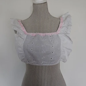 Vit handmade topp från Malicious Designs - Endast testad. Vit handsydd topp med rosa detaljer från Malicious Designs, den är en del av ''The Mary Set''. Den är ''onesize'' men uppskattar att den passar XS-M pga lite stretchig. Setet i sin helhet kostade ca 1825 kr med importmoms och frakt inräknat, men denna annonsen gäller ENDAST toppen.  Rökfritt hem men har katter.