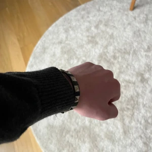 Svart armband med nitar  - Snyggt svart armband med silverfärgade nitar. Perfekt accessoar för en edgy look. Armbandet har ett spänne för justerbar passform. 