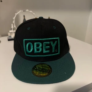 OBEY keps - Snygg svart keps med grön skärm och broderad OBEY-logga i grönt. Storlek 58cm.