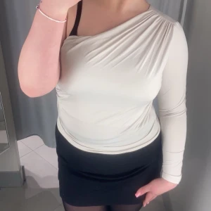 Vit oneshoulder topp - Snygg benvit oneshoulder topp med lång ärm. Toppen har en drapering över axeln och är i ett mjukt och bekvämt material. Mycket bra skick änvänd några gånger men inga skador eller fläckar på tröjan 