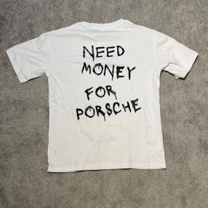 ”NEED MONEY FOR PORSCHE” T-shirt  - Vit t-shirt med svart text 'NEED MONEY FOR PORSCHE' på baksidan. Enkel design med rund hals och korta ärmar. Väldigt eftertraktad och populär. Köpt för 599kr. Helt oanvänd i orginalförpackning. Passar 165-180