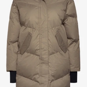 Röhnish lång dunjacka beige - En lång dunjacka med huva från Röhnish. Jackan är vattentät, har två fickor och en dragkedja framtill. Beige i Storlek XS. Inköpspris ca 2000 kr. Skön, snygg och väldigt värmande. Dragkedjan längst ned har lossnat lite ifrån jackan men det går bra at