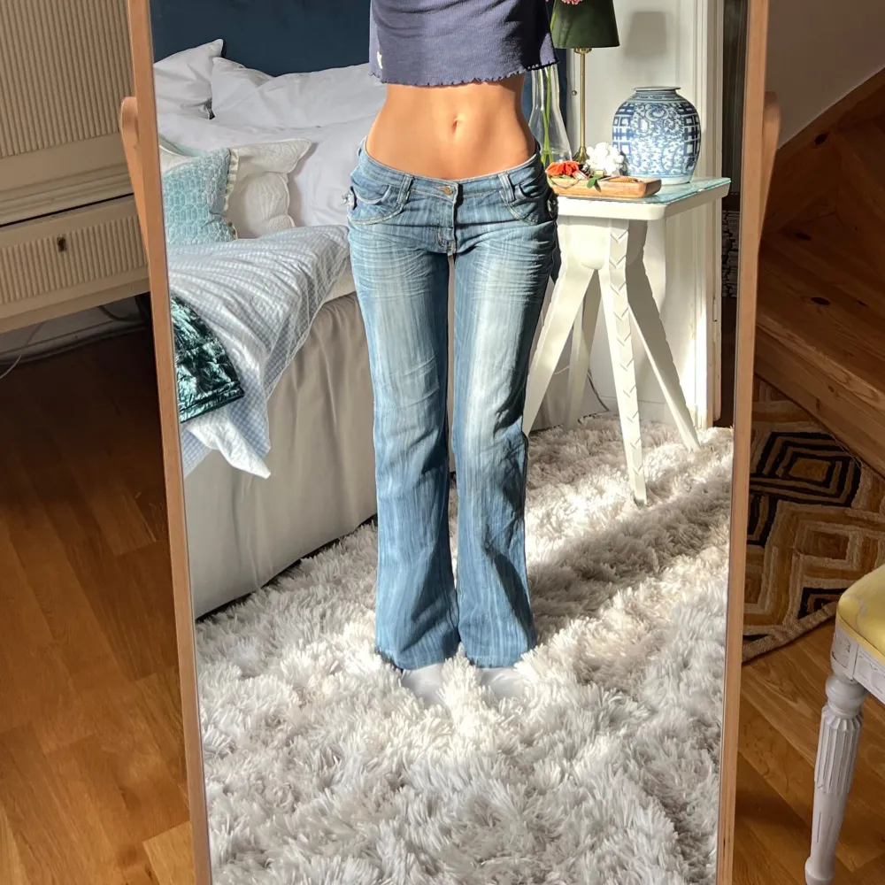 Säljer ett par snygga blå bootcut jeans med coola detaljer. De har låg midja och är dekorerade med dragkedjor och knappar på bakfickorna. Midjemått: 36cm rakt över, innerbenslängd: 80cm💋. Jeans & Byxor.